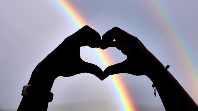 Woman Hand Making Heart Shape Against a Rainbow in the Sky in Switzerland.