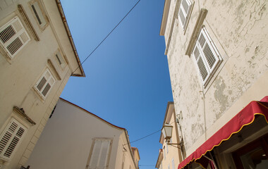 Narrow street with typical mediterranean buildings, church and blue sky at Krk, island of Krk, Croatia