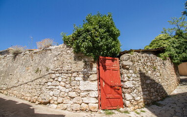 Ancient stone wall with red wooden door, green plants and blue sky at Krk, Croatia
