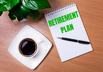 On the desktop there is a green plant, a white cup of coffee, a pen and an open notepad with the text RETIREMENT PLAN. Business concept. Close-up of the workplace.