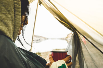 Thoughtful woman hold camping mug and drink in green tent outdoors in nature with viewpoint panorama of alpine lake in autumn - obrazy, fototapety, plakaty