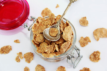 sweet dry dietary wheat muesli in a transparent glass jar and decorative spoon