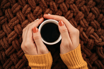 Women's hands holding hot cappuccino coffee on the background of a knitted plaid. autumn vacation concept