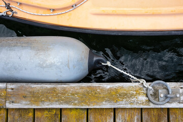 Marine fender tied with a rope to a metal ring on an old weathered pier protects the boat from...