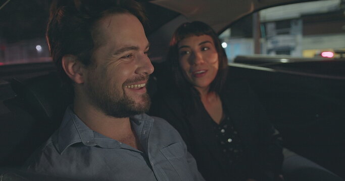 People Riding Taxi Cab Looking At Car Window At Night. Man Pointing Out Vehicle Glass With Girlfriend