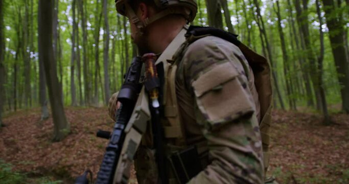 A bearded soldier stands with a weapon in the armor and helmet in the forest and looks around. Circular wiring of the camera in dynamics. Ukrainian special forces.