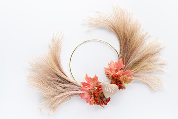 Dried floral wreath from dry pampas grass and Autumn maple leaves on metal frame. Flat lay on white...
