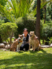 Peruvian Woman Sitting on the Grass, Hugging Two Mongrel Dogs in a Sunny Garden