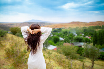 A girl in a terry, bathrobe with a towel rejoices and relaxes against the background of nature. Spa in a mountain resort. Rest in a sanatorium in the mountains. Purity and freshness of nature. - obrazy, fototapety, plakaty
