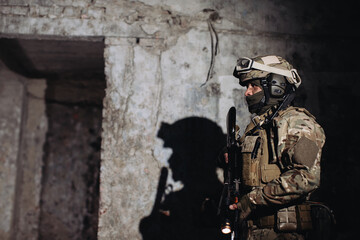 Portrait of a Ukrainian defender in the dugout. A soldier with a weapon in his hands casts a shadow on the wall.