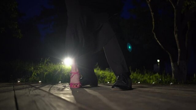 Closeup dancers legs performing latin dance on wooden support. Unknown couple feet dancing tango in dark background. Backlight, slow motion