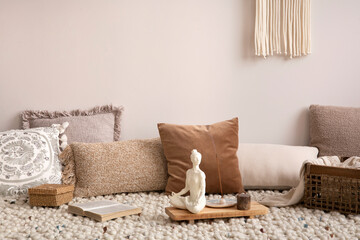 Boho and cozy interior of meditation space with a lot of pillows, plaid, hanging macrame, wooden tray with accessories, decoration, carpet and personal stuff. Warm and minimalist home decor. Template.