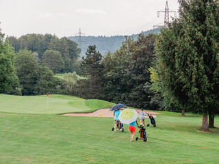 a rainy day on a golf course where golfers walk with umbrellas