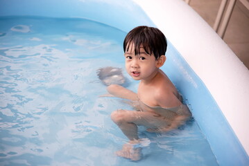 Little asian boy playing in rubber pool and looking at camera