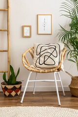 Boho and cozy interior of living room with design rattan armchair, pillows, mock up poster frame, plant, bamboo ladder, decoration and personal accessories. Stylish home decor. Template.