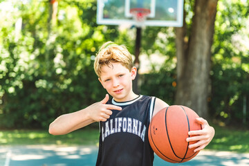 Fototapeta premium portrait of a boy kid playing with a basketball in park