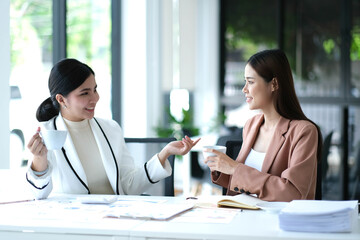Young Asian woman talk work together successfully hold coffee cups and cheers at café.