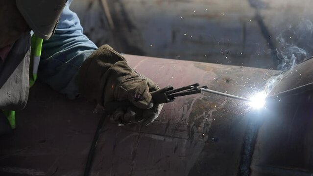 Handheld footage with a professional welder welding an industrial metallic pipeline.