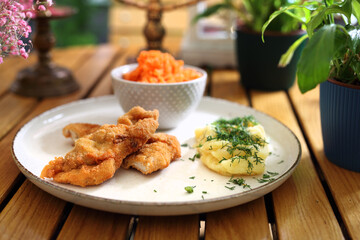 Lunch set - breaded chicken pieces, strips, potatoes with dill and a salad on a plate, on wooden table, selective focus.