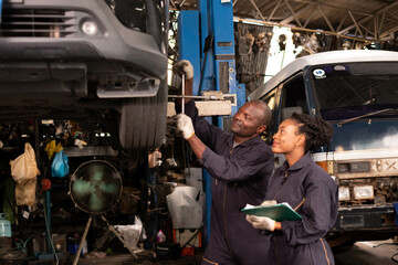 Fototapeta na wymiar African american Two mechanics - man examining car engine. Auto mechanic working in garage.Car Mechanic Detailed Vehicle Inspection. Auto Service Center Theme.