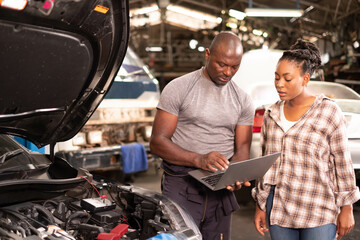 Fototapeta na wymiar African american Two mechanics - man examining car engine. Auto mechanic working in garage.Car Mechanic Detailed Vehicle Inspection. Auto Service Center Theme.