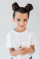 adorable girl with glitter stars on cheeks smiling while using smartphone isolated on grey.
