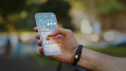 Close up of man hand using transparent mobile phone outside for calling friends. Sunny city park landscape on background. Internet connecting worldwide. Future Technology innovations.