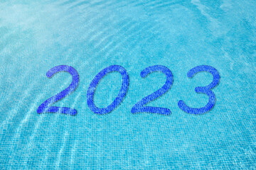 Number 2023 under blue water at the bottom of a pool. New year