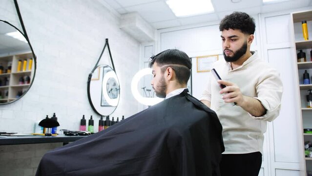 A barber with a beard cuts the man of a client sitting in a chair in a barber shop. The process of grooming a male client.