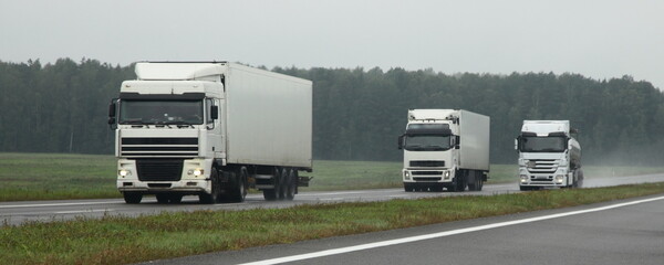 Semi trucks lorry convoy overtake on wet asphalted highway front view. Traffic safwty on rain slippery road - obrazy, fototapety, plakaty