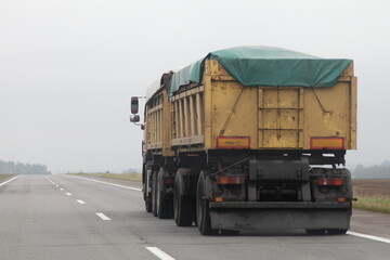 Heavy loaded yellow dump truck with tented trailer on the country highway road