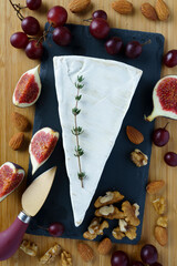 Fresh Brie cheese slice on a dark stone board with figs, red grape almonds and walnuts