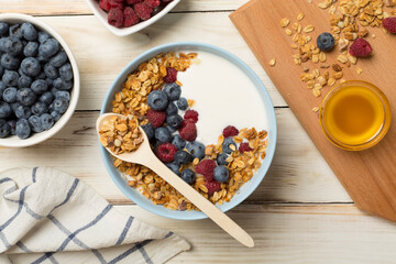 Bowl with granola, yogurt and fresh berries on wooden background, top view