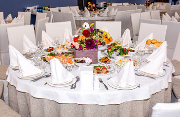 Table setting in a restaurant. Table decorated with flowers and beautiful appetizers salads on a white tablecloth. Holiday dinner.