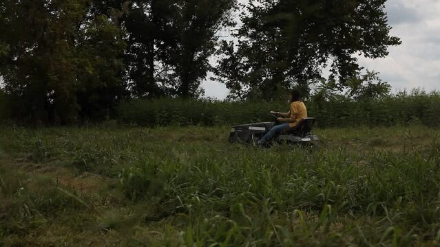 Young Female Farmer Cuts Grass on Riding Tractor Mower