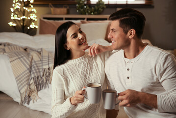 Happy couple with cups in festively decorated bedroom. Christmas celebration