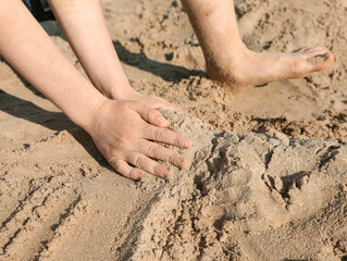 Little boy playing with sand on sunny day, closeup
