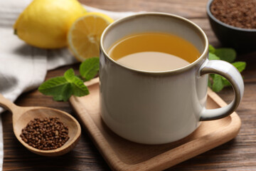 Cup of aromatic buckwheat tea and spoon with granules on wooden table, closeup