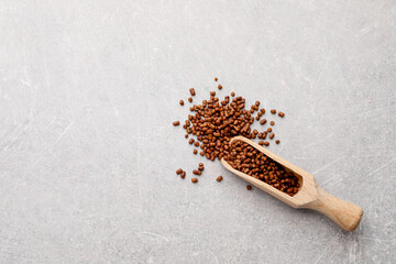 Scoop with buckwheat tea granules on light grey table, top view. Space for text