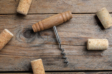 Corkscrew and wine corks on wooden table, flat lay