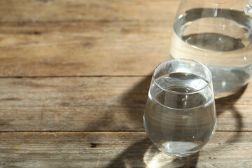 Glass of water on wooden table, space for text. Refreshing drink