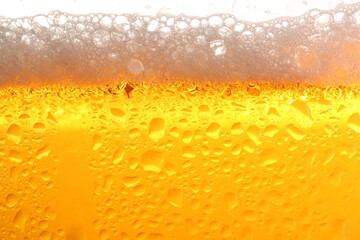 Glass of tasty cold beer with foam and condensation drops on white background, closeup