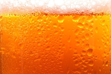Glass of tasty cold beer with foam and condensation drops as background, closeup