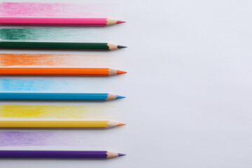 Colorful pencils with swatches on white background, top view