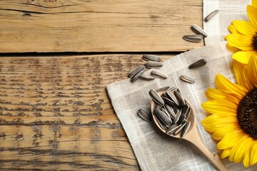 Raw sunflower seeds and flowers on wooden table, flat lay. Space for text