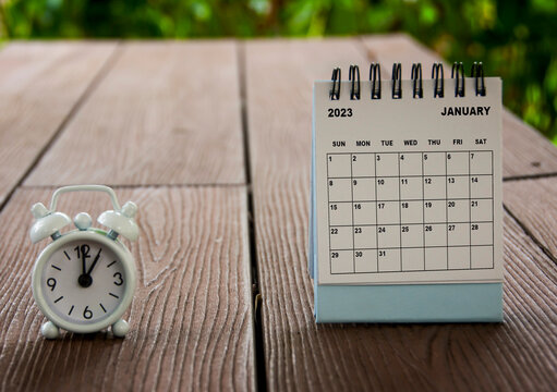 Alarm clock pointing at 1 o'clock with January 2023 calendar on a bench. Time and calendar concept