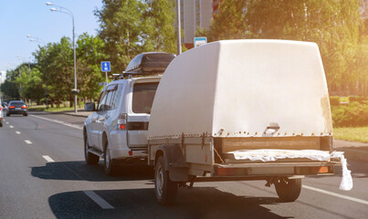 Gray car with roof rack and utility trailer on road at residential city area.