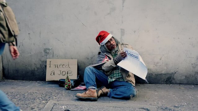 4k, A homeless man, an old Asian man wearing a red Christmas hat, is sitting on the ground reading a newspaper, next to the wall lined with job boards and many passers. Look for jobs from newspapers.