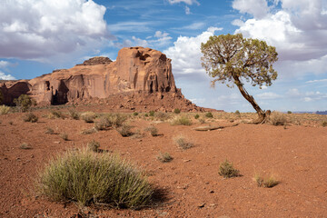 A gigantic freestanding rock in Monument Valley glows red in the afternoon sun.