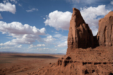 A gigantic freestanding needle like rock in Monument Valley glows red in the afternoon sun.